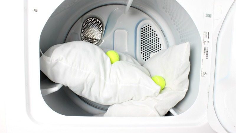 Two pillows in the dryer with two tennis balls