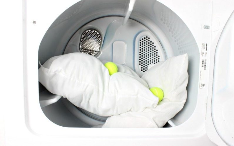 Two pillows in the dryer with two tennis balls