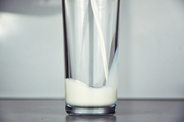 A tall and clear glass with milk being poured into it