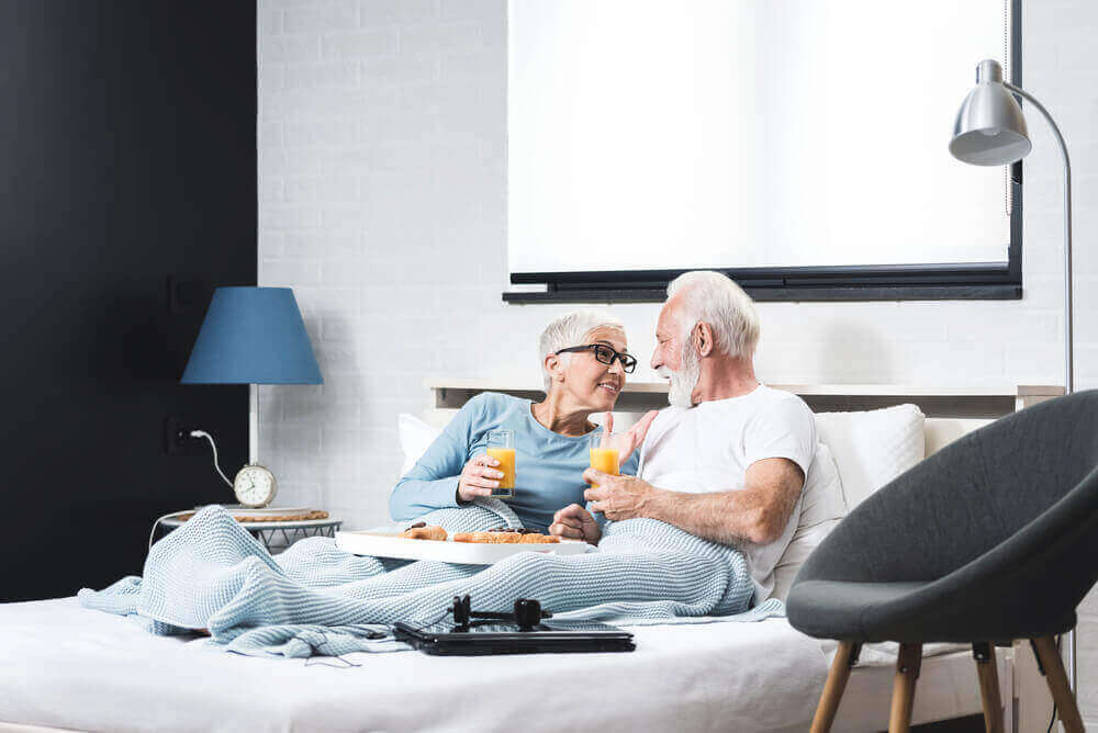 Joyful senior couple having healthy breakfast in bed in their bedroom