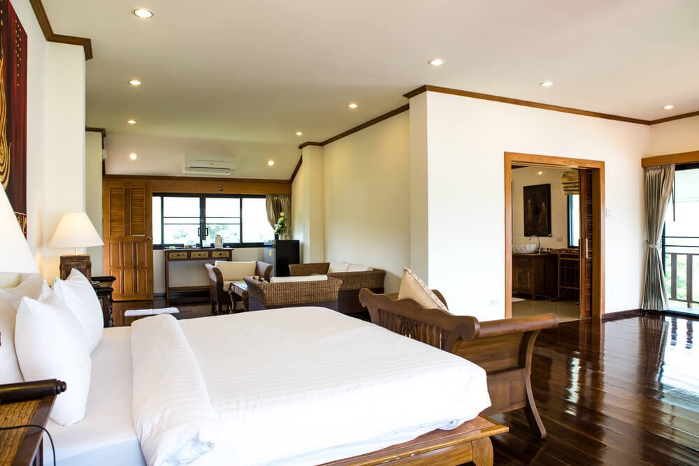 Interior of modern comfortable hotel room with a solid white hotel bed sheets and bedding wooden floors and light.