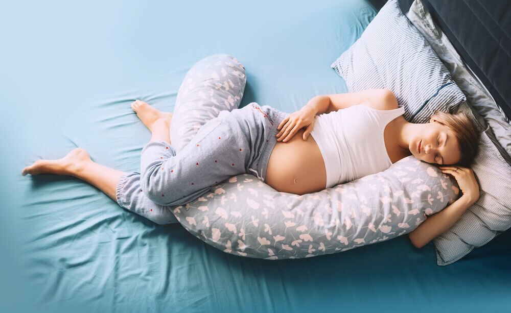 a pregnant woman resting on bed on a body pillow