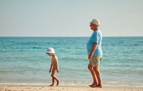 A young child and senior male walking together on beach