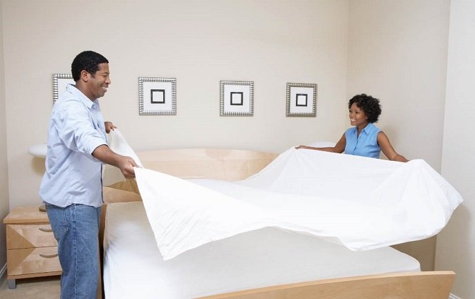 Couple making a bed with clean white sheets