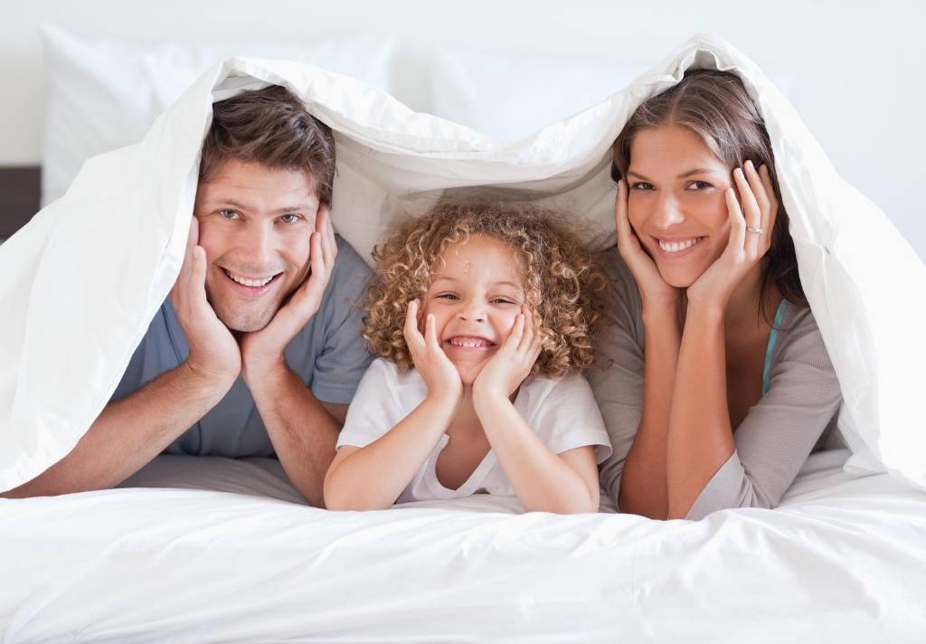 Couple and child sitting under heavy blanket on the bed
