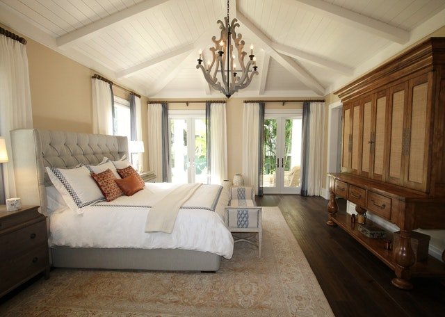 A large master bedroom with king bed and nightstands, rug under bed, large ceilings and large bay windows