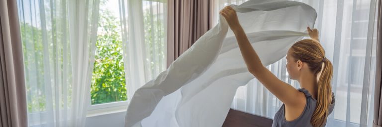 A young woman changing bedding and fitting in a fitted sheet.