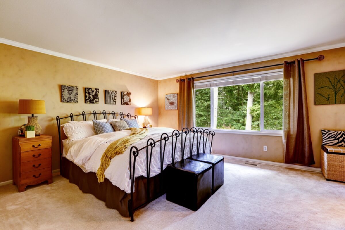 Luxury bedroom in peach color, metal bed frame, bed skirt, two leather benches at the end of bed.