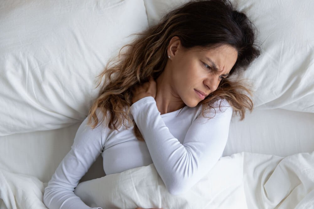 Woman with neck pain lying on pillow in bed
