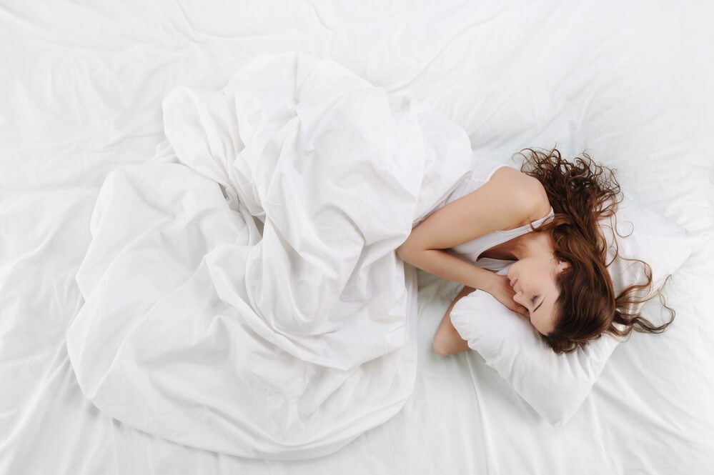 A girl sleeping on her left side on white sheets, pillows and blanket