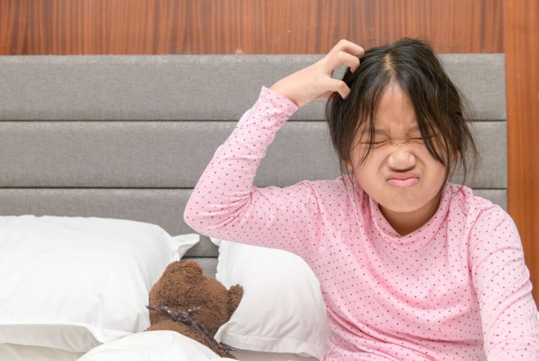 Girl with itchy her hair sitting up frustrated on bed