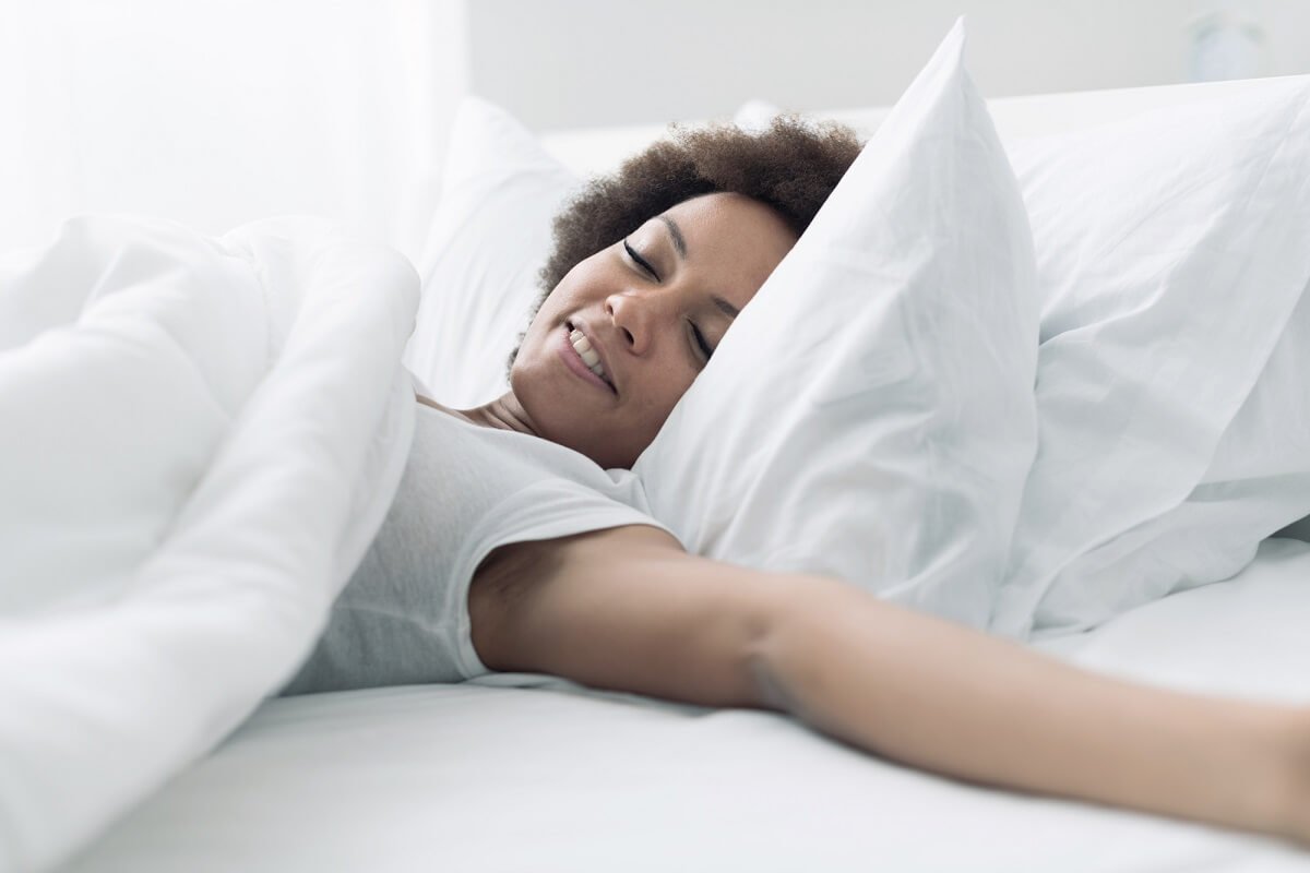 A young woman waking up in white crisp bed linen