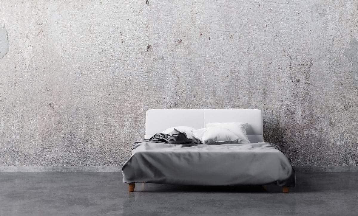 Double bed with soft clean gray satin linen and pillows in a gray colored bedroom with grunge wall.