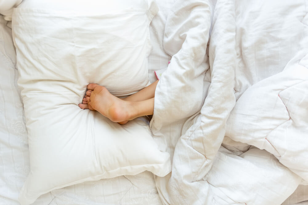 A girl sleeping on her side stomach with legs elevated using pillows