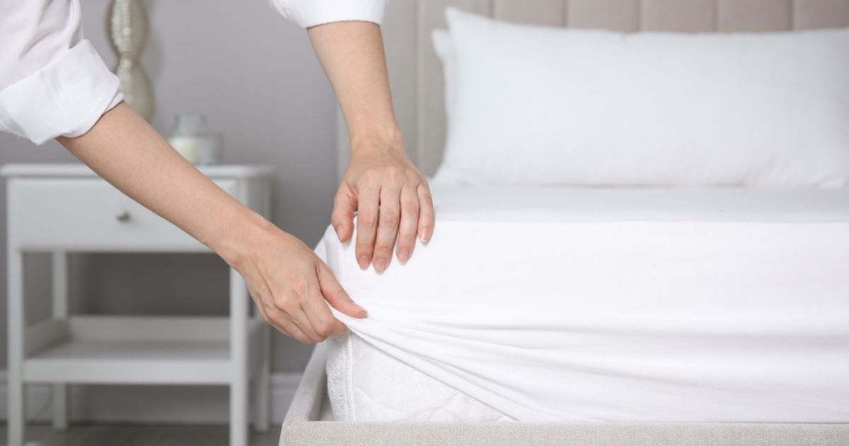A woman making a bed, putting on a fitted sheet over a thick mattress.
