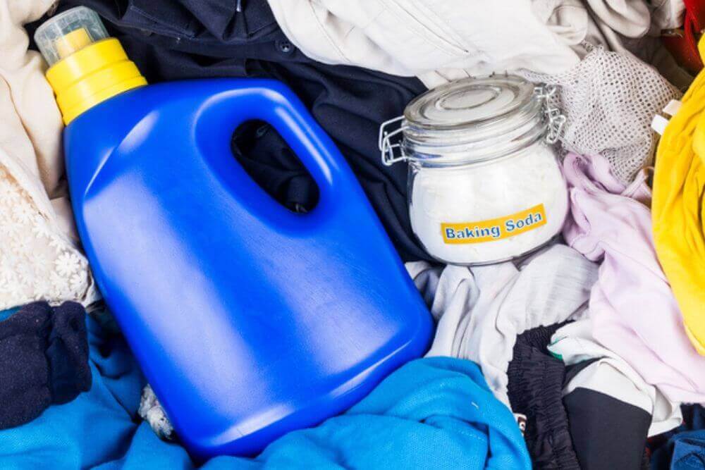 A glass jar of baking soda next to a bottle of laundry detergent on top of a pile of clothes